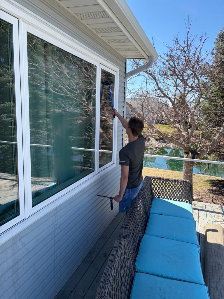 Person in black shirt standing on deck looking out large window with blue cushioned bench visible